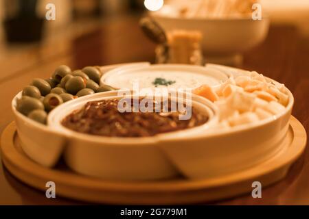 Dips of cheese, onions, olives and salsa served in bowls on a table. Blurred background. Stock Photo