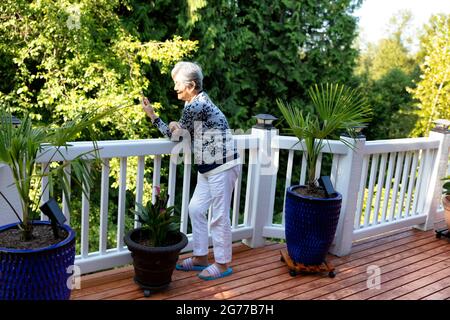 Senior woman enjoying the morning sunshine on her face while using her smartphone outdoors Stock Photo
