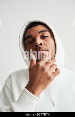 Vertical portrait of tough Latin American man wearing white hoodie and looking at camera Stock Photo