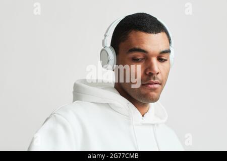 Minimal portrait of young Latin American man wearing headphones and white hoodie while listening to music, copy space Stock Photo
