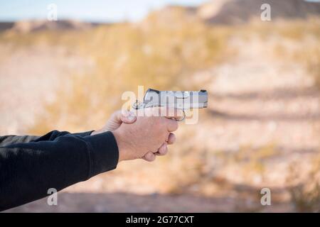 Two hands gripping on a small silver gun with a blurry background Stock Photo