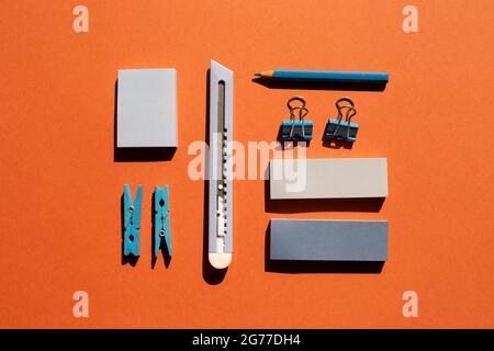Blue memo notepad, clips, cutter, colored pencil on red background. Work and study place. flat lay, top view Stock Photo