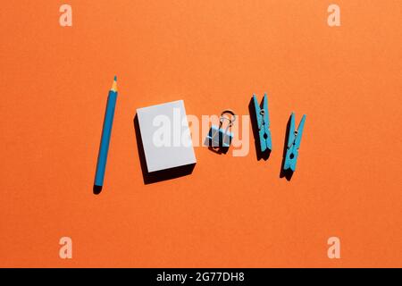 Blue memo notepad, clips, colored pencil on red background. Work and study place. flat lay, top view, copy space Stock Photo