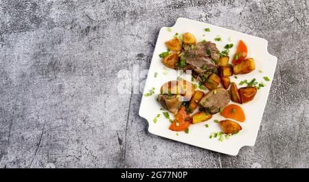 Stewed duck with baked potatoes and carrots on a square plate on a dark grey background. Top view, flat lay Stock Photo