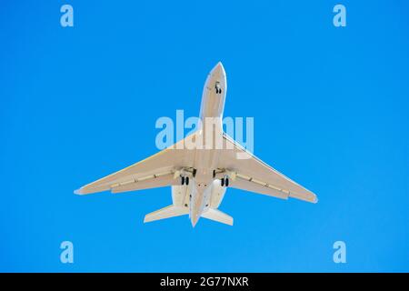 Small business jet with landing lights and deployed landing gear preparing for landing at airport. Blue sky Stock Photo