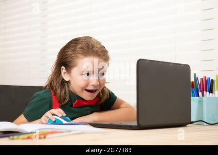 School boy with a happy smiling face studying and using computer laptop and writing on notebook. Nerd funny pupil. Stock Photo