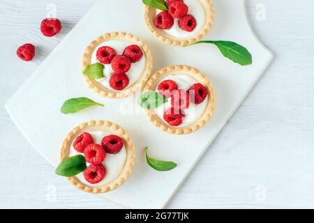 Tartlets with cream and raspberry on a white wooden board Stock Photo