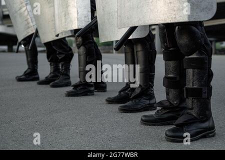 Group of riot police staff in black boots standing on asphalt at street and holding shields Stock Photo