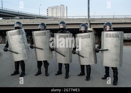 Group of police guard in helmets holding side-handle baton and metal shields standing in row at street Stock Photo