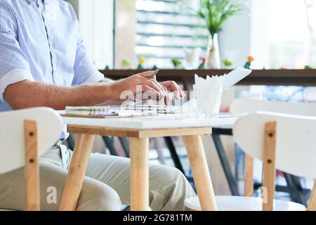 Hands of man working on laptop at cafe table and taking notes in planner Stock Photo