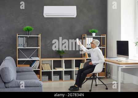 Senior businessman holding a remote control aimed at adjusting the air conditioner. Stock Photo