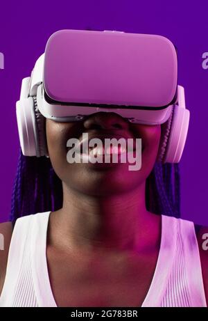 Futuristic closeup portrait of young African-American woman wearing VR headset against purple background Stock Photo