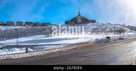 A church in a field covered in snow and a few houses beside it Stock Photo