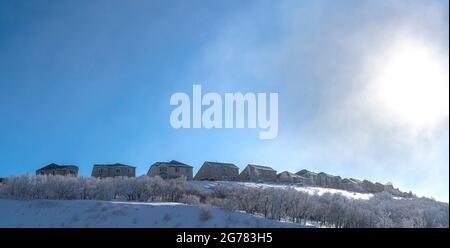 Clear, bright and sunny on a winter day shining on a field covered in snow with a row of houses on the background Stock Photo
