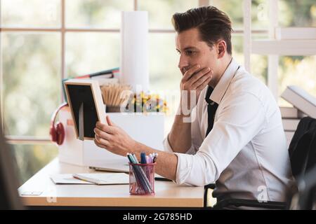 Young Caucasian businessman sits alone near the belonging box and feels stressed looking for photo frame of his family with hopeless and shock after g Stock Photo