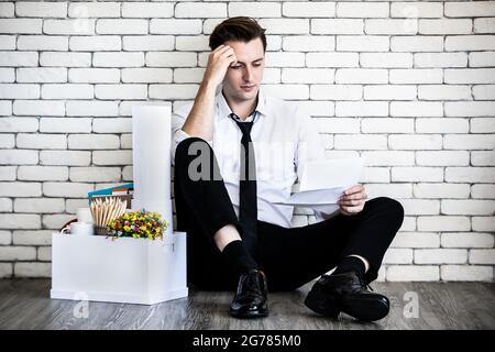 Young caucasian businessman tired sitting with feel sad, stressed and unhappy face holding fired notice letter beside box of belongings collected from Stock Photo