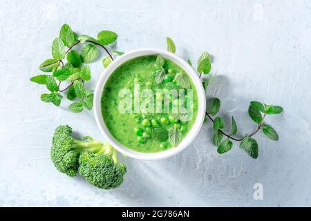 Vegan soup with green peas, broccoli and fresh mint leaves, top flat lay shot. Healthy detox puree. Organic vegetable diet, spring recipe Stock Photo