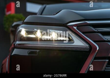Front illuminated headlights of a black luxury modern car. Close up detail on one of the LED headlights with flare of modern car Stock Photo