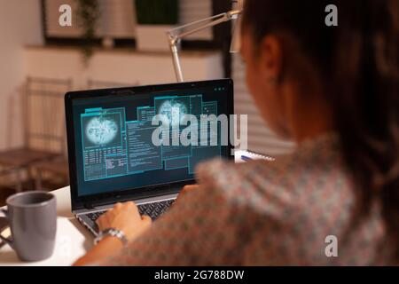 Woman doing cyberspace criminal activity hacking firewall using laptop from home office at night time. Programmer writing a dangerous malware for cyber attacks using performance laptop during midnight. Stock Photo