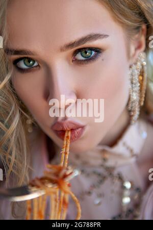 Lovely girl eating pasta (spaghetti). Close-up portrait of a beautiful young woman Stock Photo