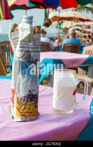 Bottle of Kingfisher and beer glass, Kerala is a dry state so alcohol is served at beach bars with a paper covering and hidden under the table, India Stock Photo