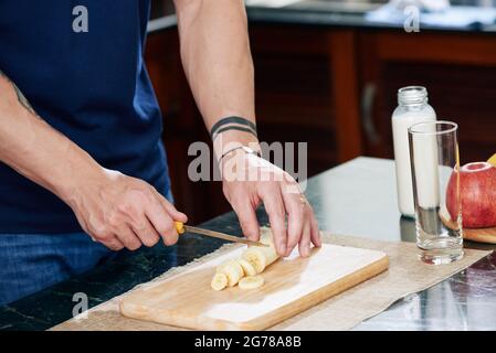 Hands of muscular man cutting fresh banana when making delicious healthy high calorie cocktail Stock Photo