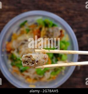 Top view close up hand hold chopsticks pick up fried spring rolls on vegan rice noodles serving from order online in plastic bowl Stock Photo