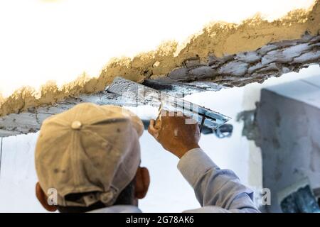 Worker plastering cement mortar on concrete ceiling beam with trowel Stock Photo