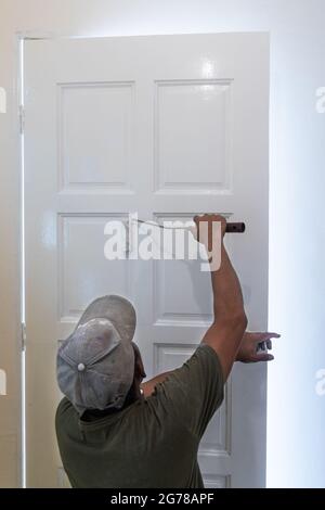 Person painting wooden white door with paint roller during home rennovation Stock Photo