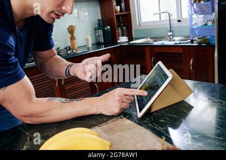 Cropped image of fit man counting ingredients of green smoothie recipe on screen of tablet computer Stock Photo
