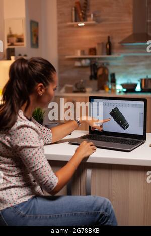 Engineer pointing at turbine project on laptop while working on laptop during night time. Industrial female engineer working on personal computer showing cad software. Stock Photo