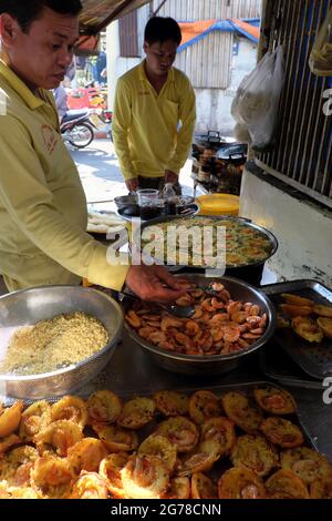 HO CHI MINH CITY, VIET NAM- JAN 5, 2020: Two Vietnamese man making mini shrimp pancake on pavement at sidewalk restaurant, yellow crispy cake in cooki Stock Photo