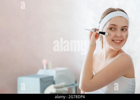 Young woman apply clay face mask. Teenage girl spreads clay mask on cheek with brush at home in bathroom. Self Care Beauty skincare spa and treatment Stock Photo