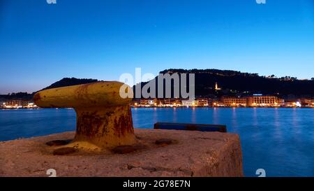 Zakynthos, Zakynthos City, night shot, evening shot, harbor, yellow pier in the foreground, night skyline of Zakynthos City in the middle distance, castle hill in the background, blue night sky, illuminated church tower of Agias Triadas Stock Photo