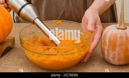 Woman hands making pumpkin puree using an electric blender. Pumpkin puree recipe, lifestyle, rustic backround Stock Photo