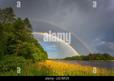 Rainbow over stormy sky. Rural landscape with rainbow over dark stormy sky in a countryside at summer day. Stock Photo