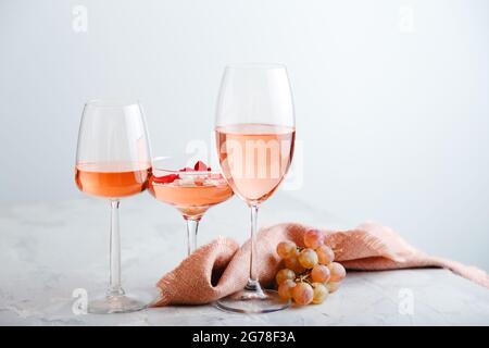 Rose wine in different types of glasses on light grey concrete background with grapes. Rose Wine composition on white table. Stock Photo