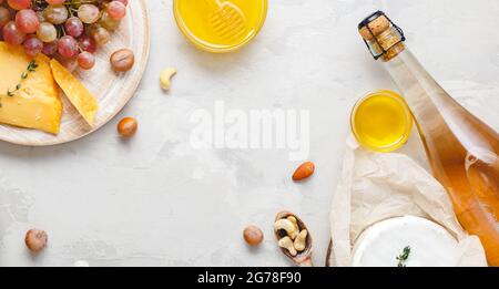 Wine composition on light gray rustic concrete background. Frame made of pink rose wine bottle cheese nuts and grapes honey. Camembert cheese, wine Stock Photo