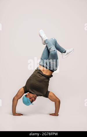 Hispanic dancer with casual clothes doing handstand and dancing in studio shot against white background. Stock Photo
