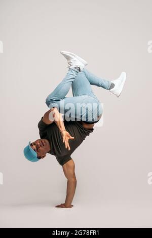Hispanic dancer with casual clothes doing handstand and dancing in studio shot against white background. Stock Photo