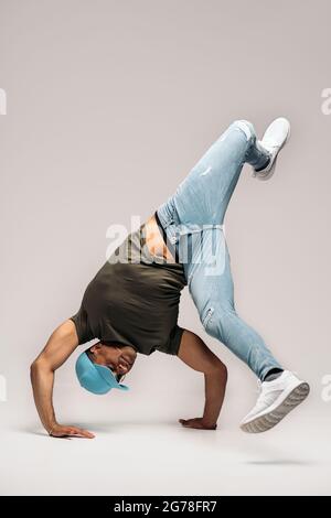 Hispanic dancer with casual clothes doing handstand and dancing in studio shot against white background. Stock Photo