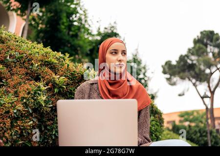 Young muslim woman with head scarf using her computer in the park. Stock Photo