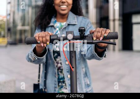 Happy black woman with her nails done using electric scooter in the city. Stock Photo