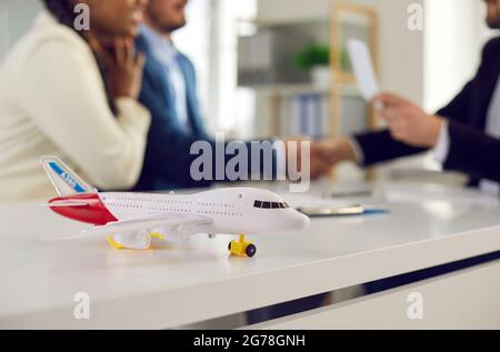 Close up of little model airplane on table on background of happy couple in travel agency office. Stock Photo