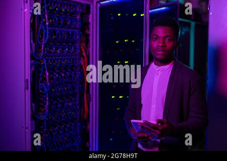 Portrait of serious young Afro-American datacenter engineer using digital tablet while checking server connection Stock Photo