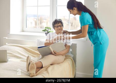 Woman nurse giving prescribed pills and glass of water to happy elderly lady Stock Photo