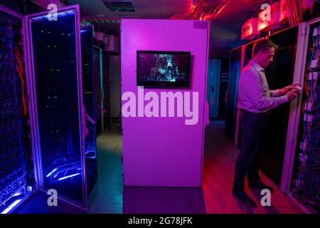 Concentrated mature IT engineer using wireless device while administrating network system in data center with neon light illumination Stock Photo