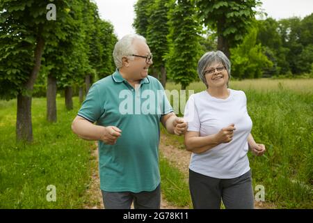 Happy active elderly couple on a summer day jogging outdoors in a park or forest. Stock Photo
