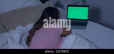 Young woman lies on the bed with her laptop - green screen display Stock Photo