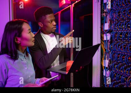 Serious young multi-ethnic colleagues discussing internet connection while working together at data center Stock Photo